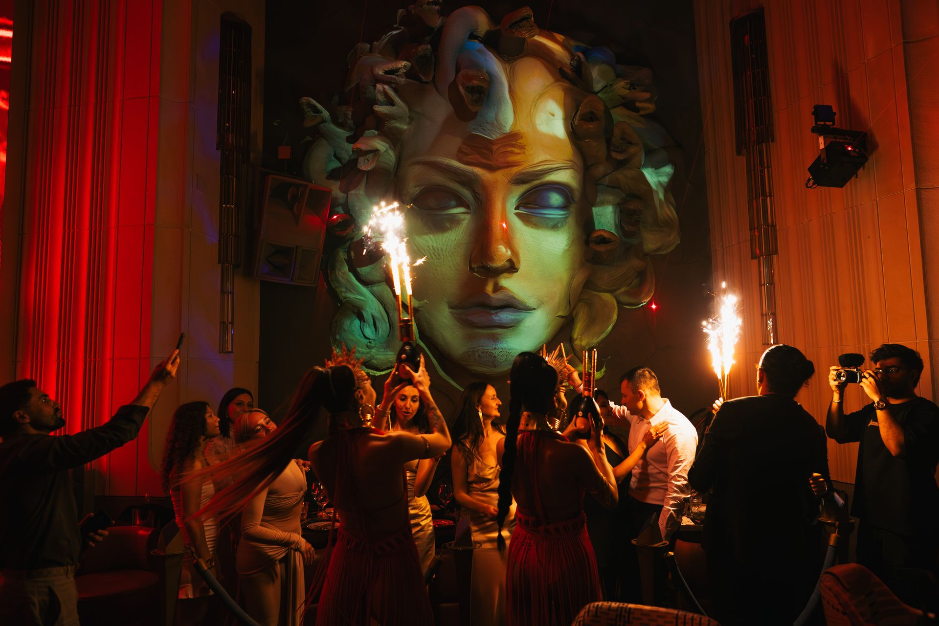 Guests raising sparkler bottles beneath the golden Medusa at midnight