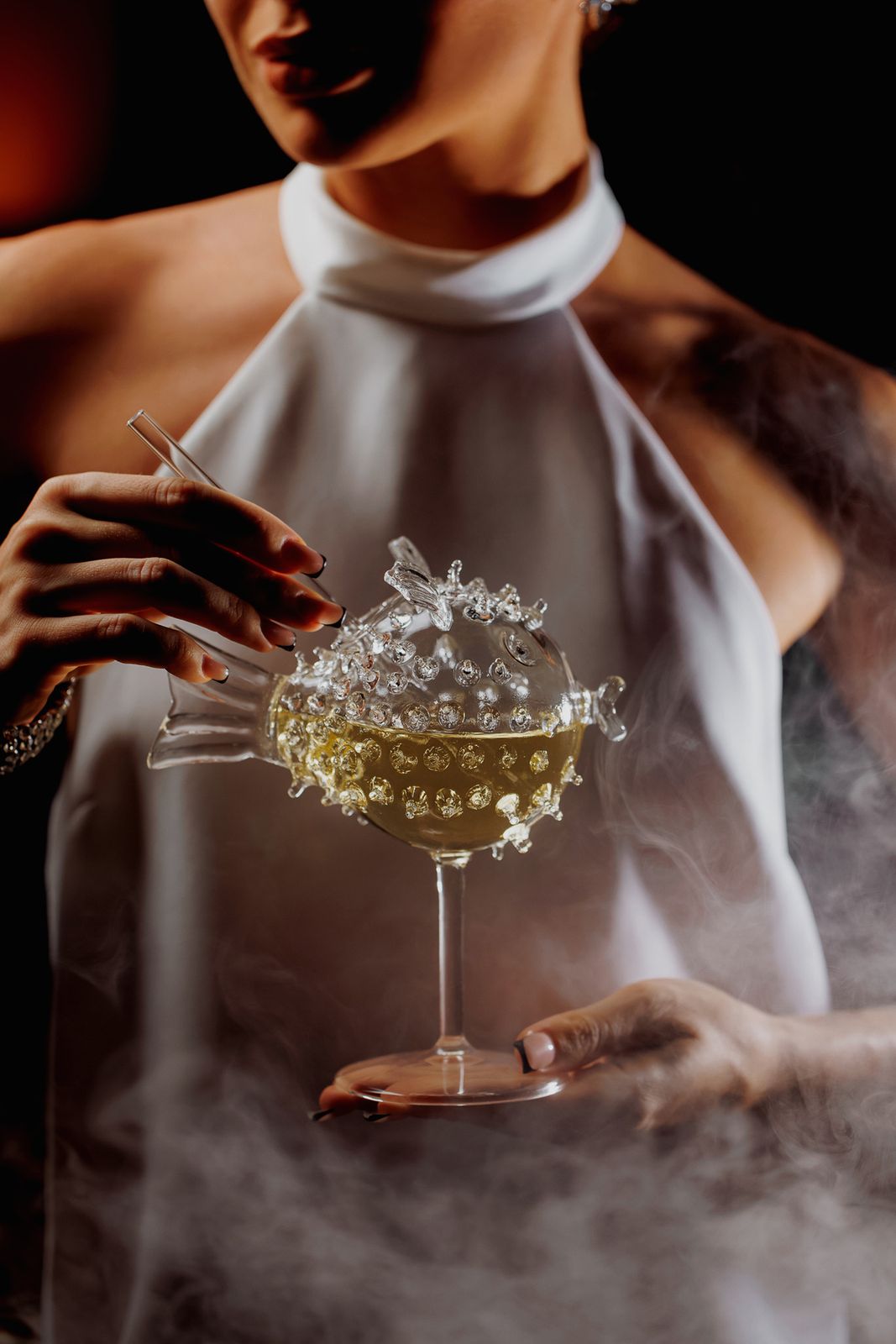 A guest in white holding a smoking pufferfish glass