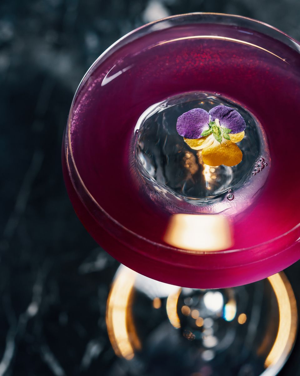 A violet cocktail with an edible flower, seen from above