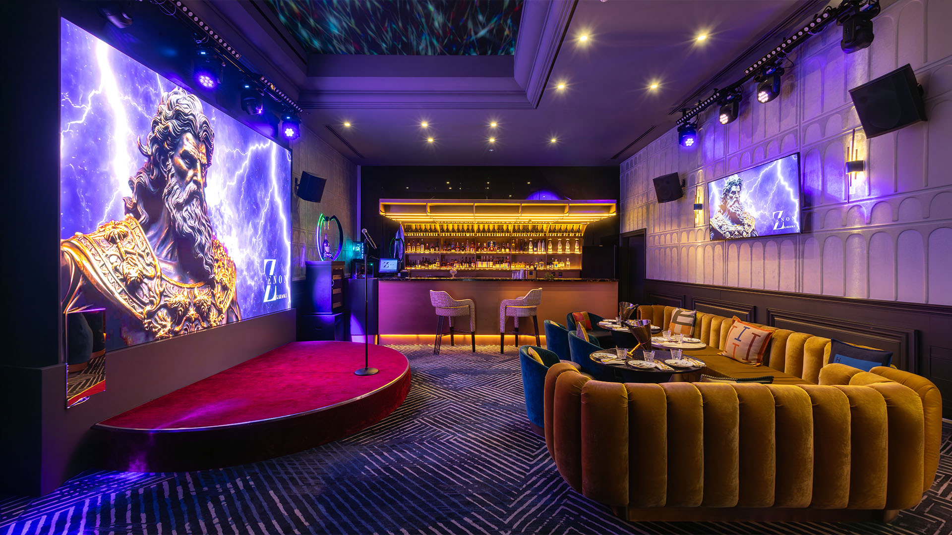 The karaoke hall, wide view: stage with microphone, LED screen, bar and sofas