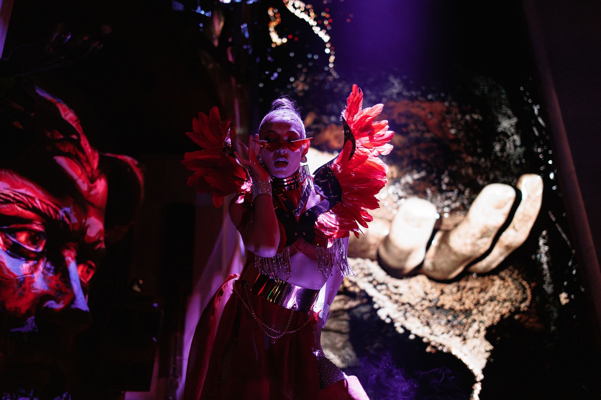 A performer in red feathers beside the giant stone hand